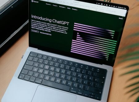 A sleek laptop on a wooden desk showing the ChatGPT homepage by a window.